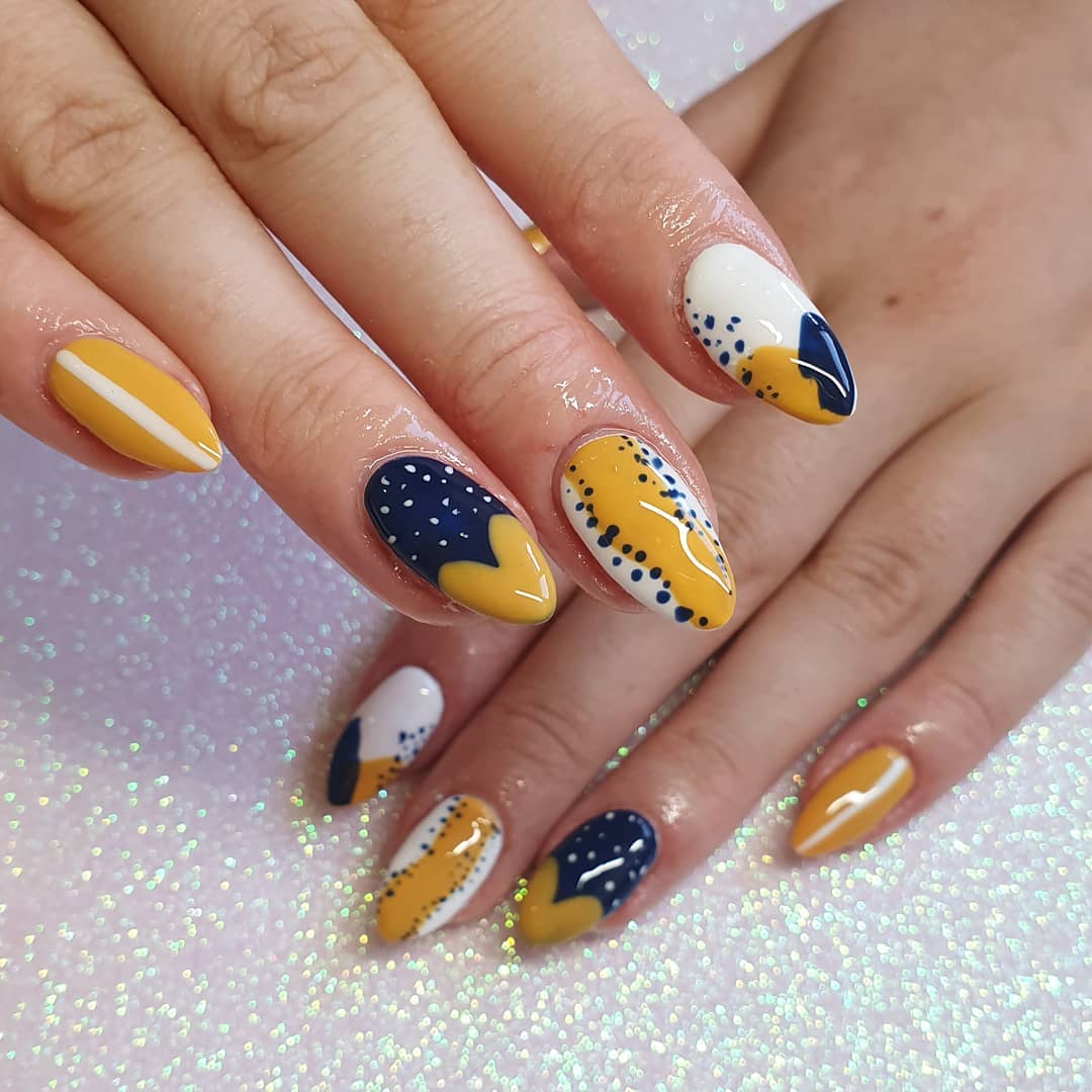 Uñas en almendra con arte abstracto en mostaza, azul marino y blanco con puntos